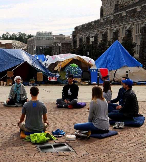 A picture of students with Holly Rogers sitting in meditation while waiting for tickets to a Duke Basketball game